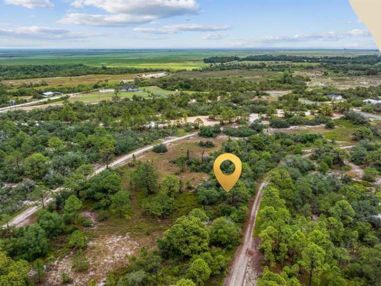 Aerial view of a parcel in Sun 'N Lake Estates, Lake Placid, marked with a map pin, showing sandy scrub and pine flatwoods with graded sand roads and open agricultural land on the horizon.